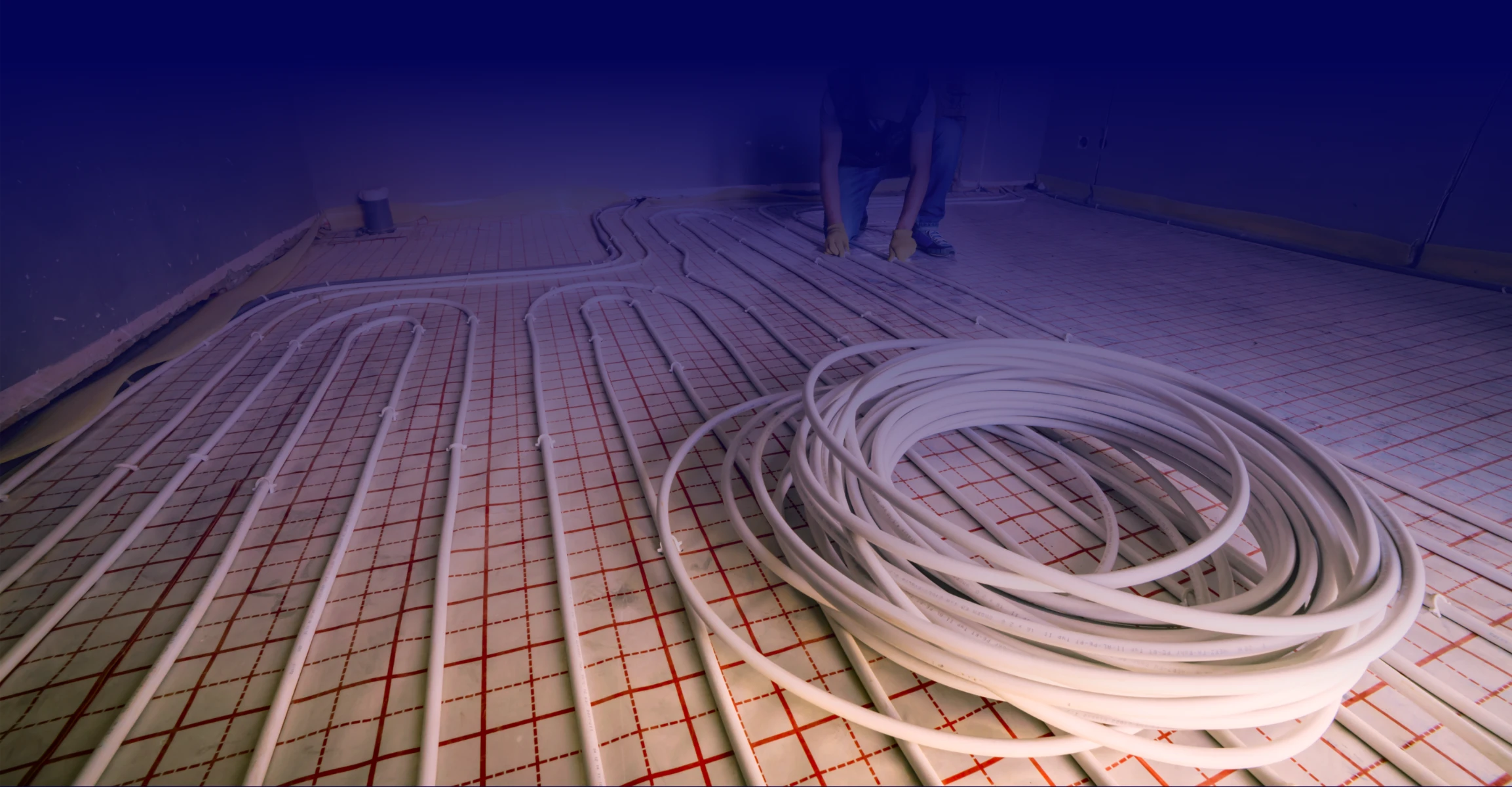 Białe rurki ułożone na czerwonej macie przygotowane pod ogrzewanie podłogowe wodne