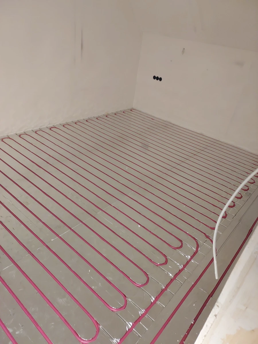 Rozłożone pętle różowych rur ogrzewania podłogowego wodnego na warstwie izolacji