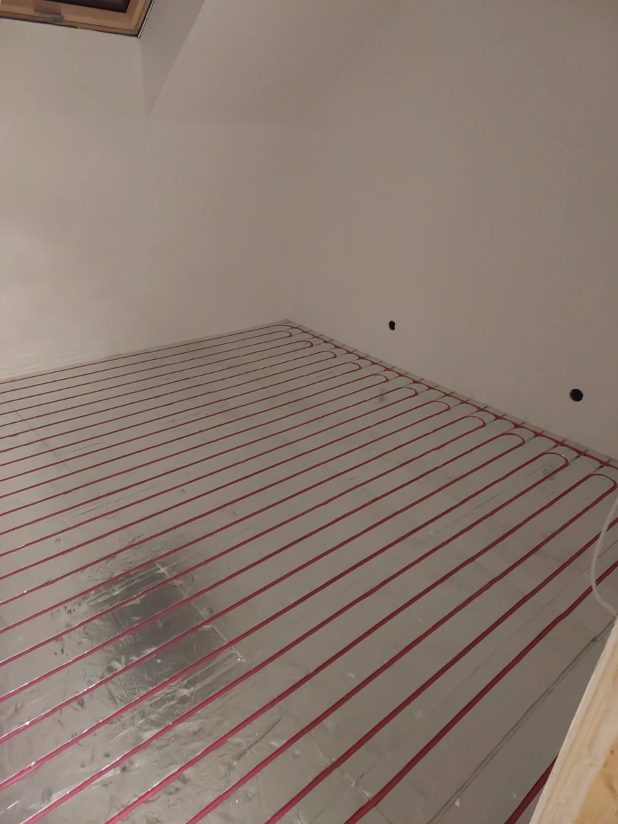 Rozłożone czerwone rurki ogrzewania podłogowego wodnego na izolacji i folii aluminiowej przed wylewką