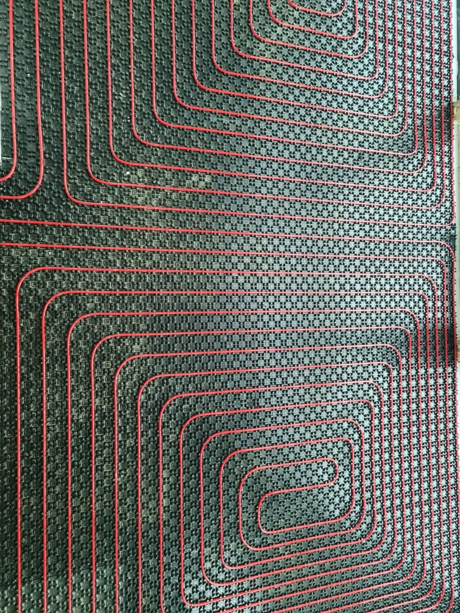 Czerwone rurki ułożone w pętle na czarnej płycie izolacyjnej pod ogrzewanie podłogowe wodne