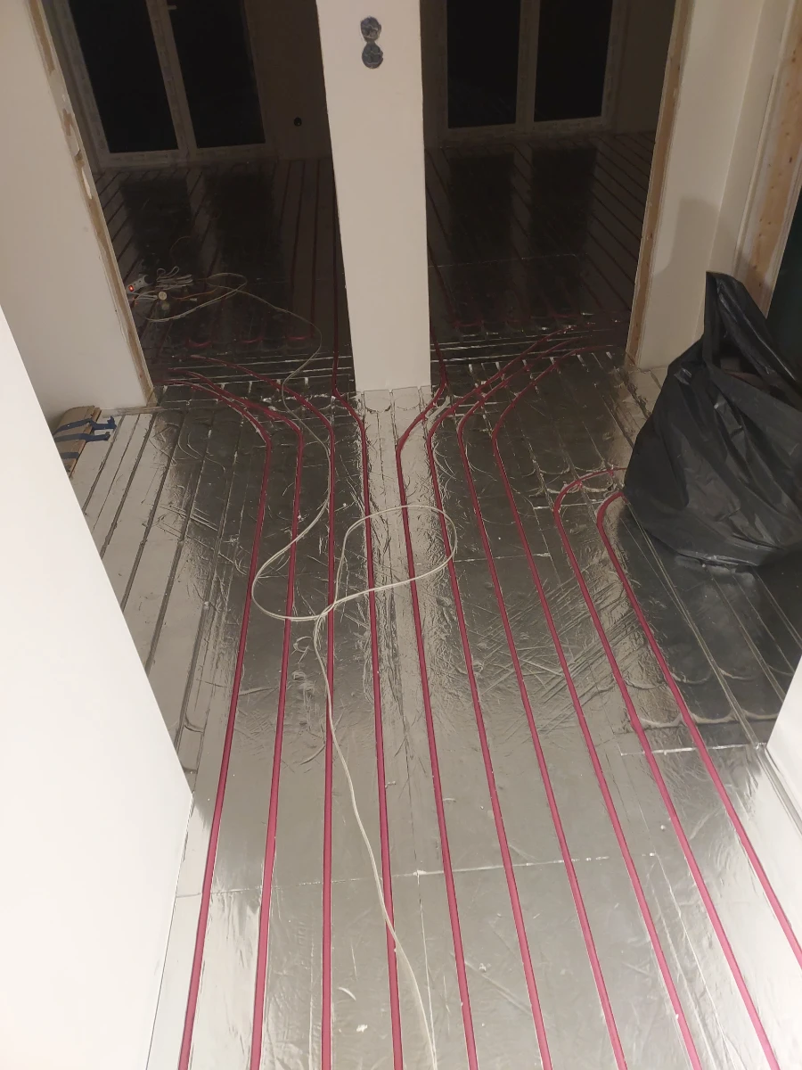 Montaż ogrzewania podłogowego wodnego – czerwone rury ułożone na izolacyjnej folii